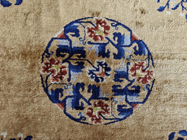 Textured tan rug with a prominent circular floral motif detailed in dark blue and rust.