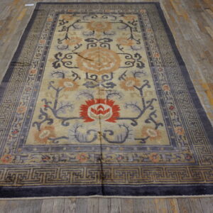Tan field rug with gray, orange, and red floral designs and a dark key border on rustic wood planks.