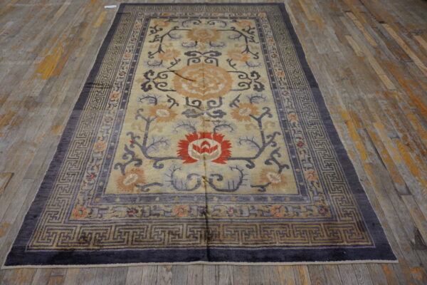 Tan field rug with gray, orange, and red floral designs and a dark key border on rustic wood planks.