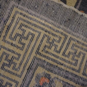 Close-up of a low-pile rug corner with a gray and tan geometric meander pattern.