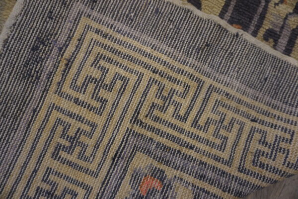 Close-up of a low-pile rug corner with a gray and tan geometric meander pattern.