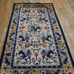 Rectangular blue and beige rug with Foo dog pattern and thick borders on distressed wood planks.