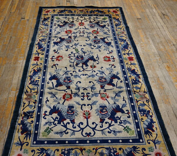 Rectangular blue and beige rug with foo dog pattern and thick borders on distressed wood planks.