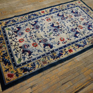 Rectangular low-pile rug with a cream field, blue floral and lion pattern, and thick blue and gold border on wood flooring.