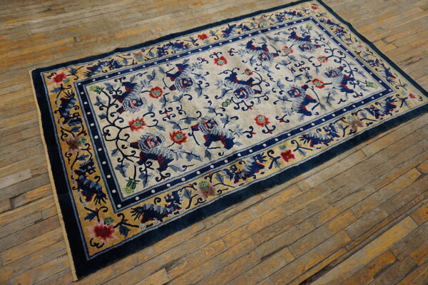 Rectangular low-pile rug with a cream field, blue floral and lion pattern, and thick blue and gold border on wood flooring.