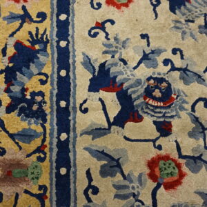 Textured cream rug with bold navy blue, gold, and red floral and mythical creature motifs near a dark blue border.