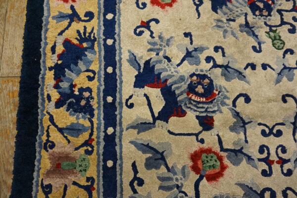 Textured cream rug with bold navy blue, gold, and red floral and mythical creature motifs near a dark blue border.