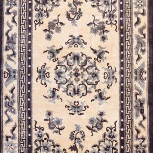 Cream rug with navy blue floral patterns and geometric borders lies on glossy hardwood flooring.