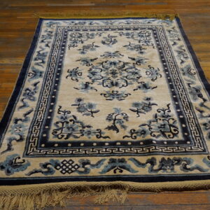 Traditional cream rug with dark blue floral and geometric patterns, framed by fringe on wood plank floors.