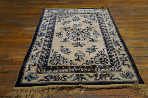 Traditional cream rug with dark blue floral and geometric patterns, framed by fringe on wood plank floors.