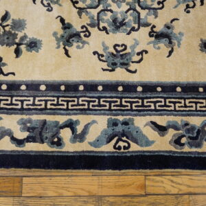 Textured cream rug with dark blue floral and Greek key borders placed over light wood planks.