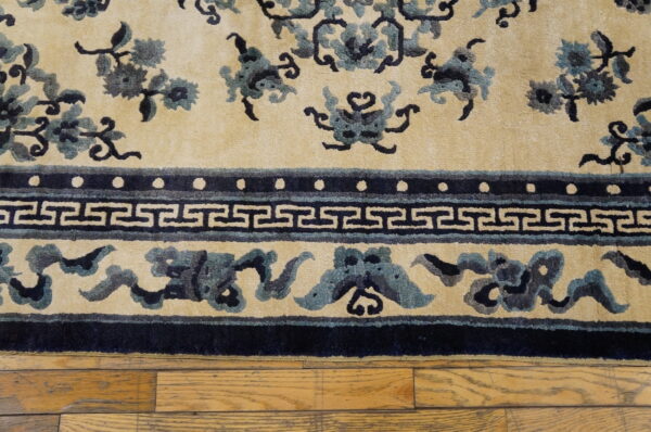 Textured cream rug with dark blue floral and greek key borders placed over light wood planks.