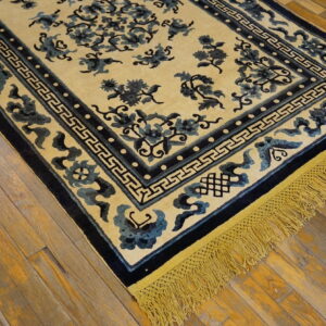 Pale yellow rug featuring blue floral motifs, dark borders, and bright fringe, displayed on distressed wood planks.