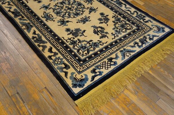 Pale yellow rug featuring blue floral motifs, dark borders, and bright fringe, displayed on distressed wood planks.