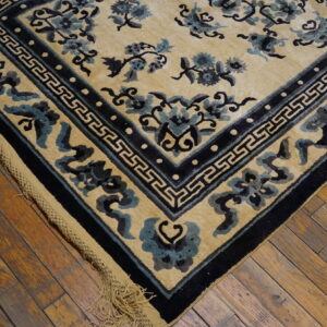 Close-up of a tan rug with dark blue sculpted floral patterns and geometric borders on wood floor.