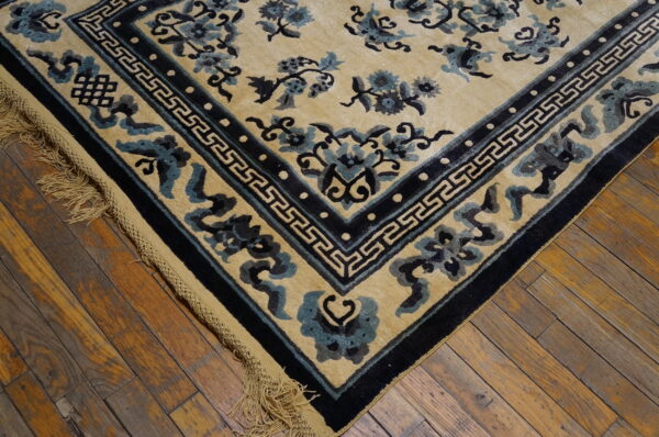 Close-up of a tan rug with dark blue sculpted floral patterns and geometric borders on wood floor.