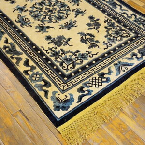 Light yellow rug with dark blue floral patterns, a geometric border, and golden fringe on rustic wood planks.