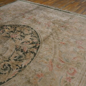 Close-up of a low-pile traditional rug with a dark green medallion and beige floral pattern on wood floor.