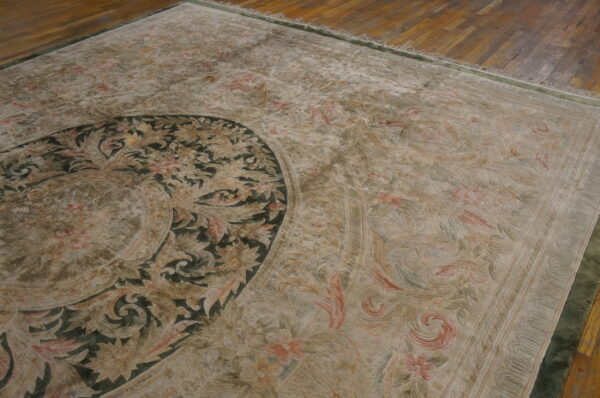 Close-up of a low-pile traditional rug with a dark green medallion and beige floral pattern on wood floor.