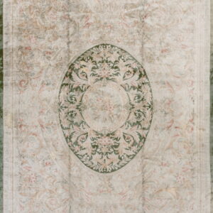 Ornate classical rug in pale cream and blush tones with a central dark green oval floral medallion.
