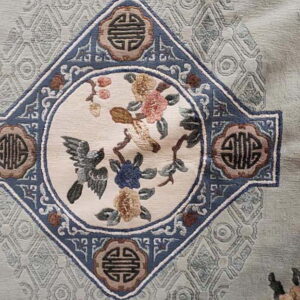 Detail of a pale green rug featuring a blue medallion with birds, pink, and gold floral motifs.