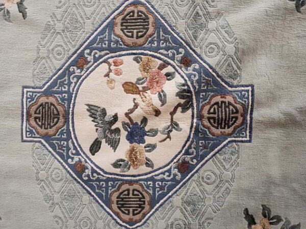 Detail of a pale green rug featuring a blue medallion with birds, pink, and gold floral motifs.