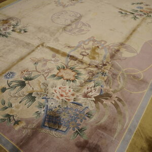 Lustrous beige rug displays detailed floral motifs and mauve accents on a rustic wood floor.