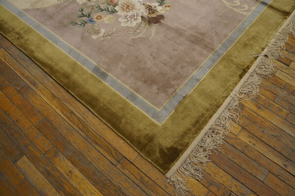 Low-pile rug with mauve floral field and plush olive green border lies on distressed hardwood flooring.