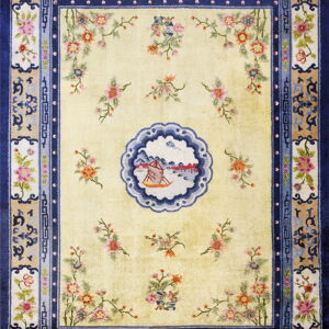Light yellow rug featuring scattered florals and a scenic medallion within detailed navy and tan borders.