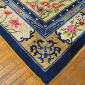 Floral and geometric patterned rug corner in navy blue, pink, yellow, and tan on worn wood flooring.