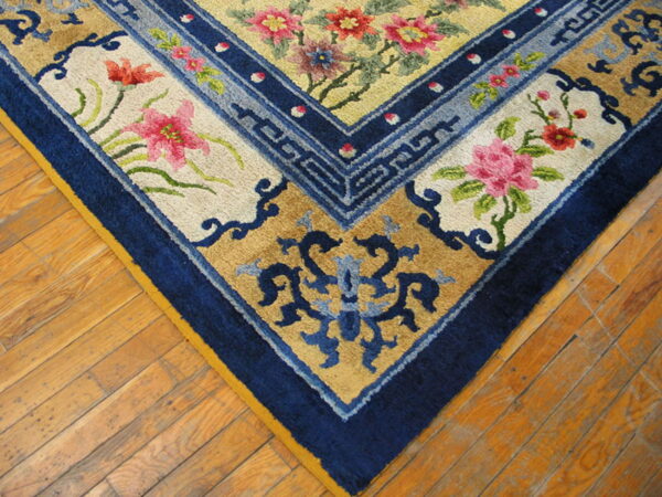 Floral and geometric patterned rug corner in navy blue, pink, yellow, and tan on worn wood flooring.