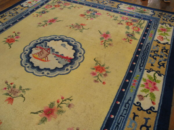 Low pile rug featuring a yellow field, pink flowers, and elaborate blue geometric and floral borders.