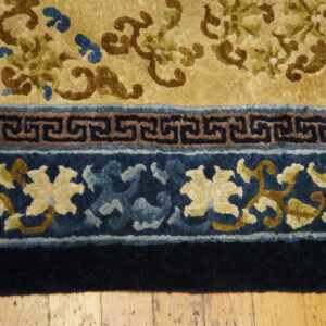 Golden yellow rug detail showing brown and green floral patterns and a dark blue fret and floral border.