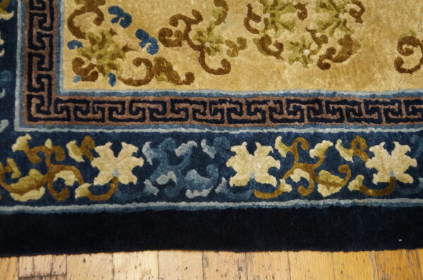 Golden yellow rug detail showing brown and green floral patterns and a dark blue fret and floral border.