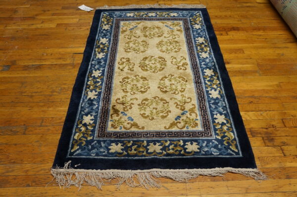 Navy and tan rug featuring scrollwork medallions and detailed blue borders rests on a plank hardwood floor.