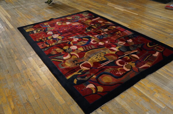 Sculpted abstract rug with red, yellow, and blue colors, bordered in black on rustic wood flooring.