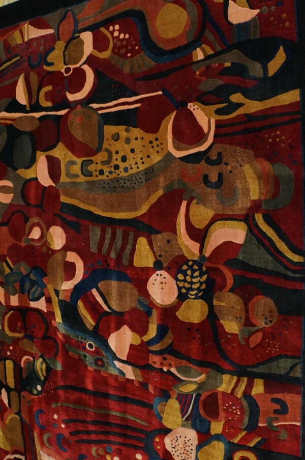 A deeply carved rug with an abstract pattern of organic forms in maroon, mustard, dark blue, and pink.