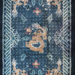 Navy blue rug with a textured tan dragon pattern and a blue and white interlocking geometric border.