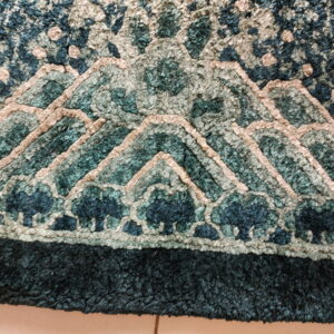 Close-up of a dimensional looped rug featuring an abstract mountain design in shades of teal and beige.