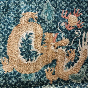 Tan dragon motif with coral accents stands out on a highly textured, mottled teal and blue rug.