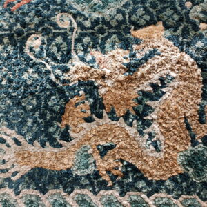 Close-up of a textured blue and tan rug featuring a shaggy mythological dragon pattern.