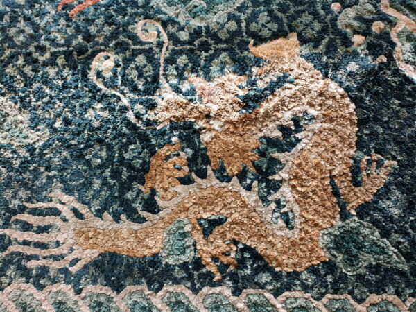 Close-up of a textured blue and tan rug featuring a shaggy mythological dragon pattern.