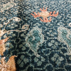 Textured deep teal rug close-up showing dimensional scrolling patterns in peach, beige, and sage high pile.
