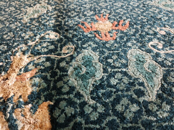 Textured deep teal rug close-up showing dimensional scrolling patterns in peach, beige, and sage high pile.