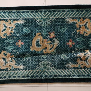 Dark teal high-low pile rug featuring raised gold dragon patterns and a geometric border on white tile.