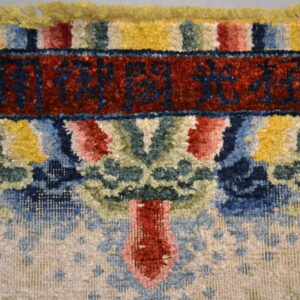 Close-up of a high pile rug showing colorful abstract pattern, yellow fringe, and a red field with dark script.