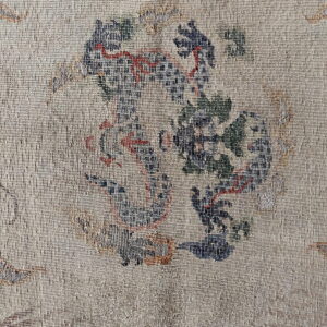 Low-pile beige rug with tightly woven stylized motifs in deep blue, terracotta red, and muted green.