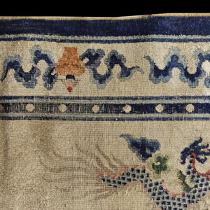 Distressed rug detail showing a beige ground, stylized blue waves, and dark navy polka dot borders.