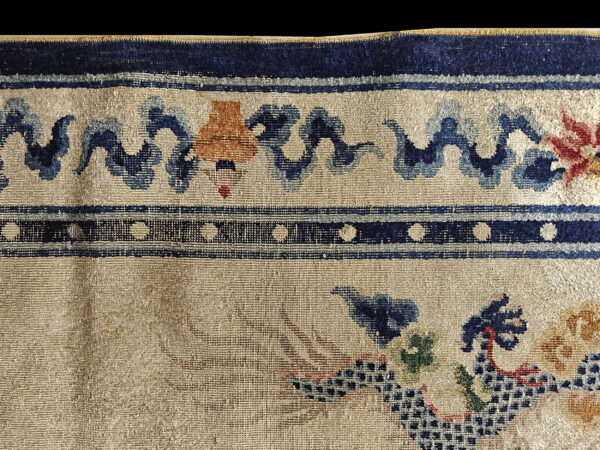 Distressed rug detail showing a beige ground, stylized blue waves, and dark navy polka dot borders.