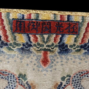 High-pile rug detail shows a colorful border, a red cartouche with script, and a beige patterned field.